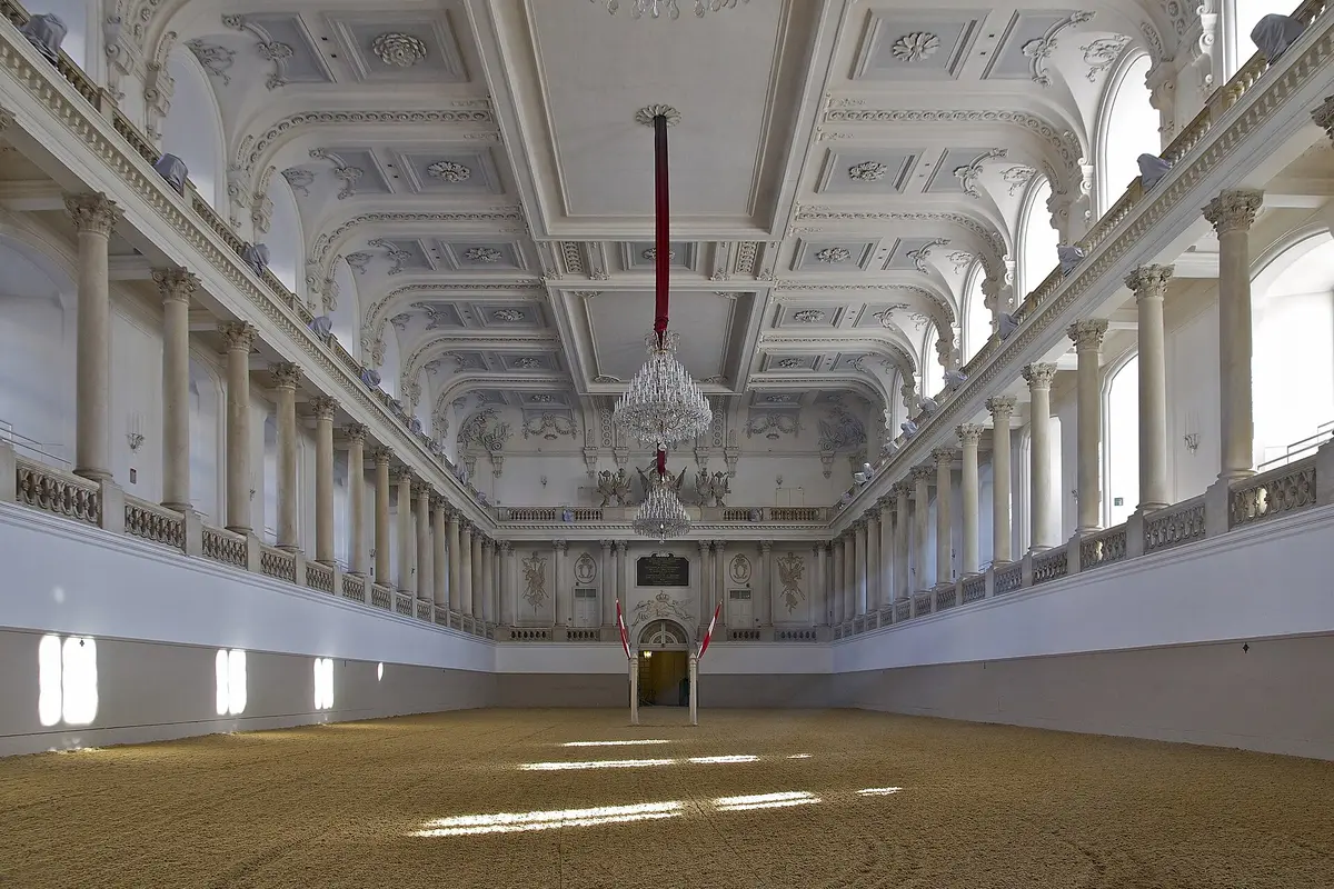 Der weiße Barocksaal der Winterreitschule in Wien mit zwei Stockwerken aus Säulen und Galerien, Stuckdecken, Kronleuchtern und einem Sandboden in der Arena